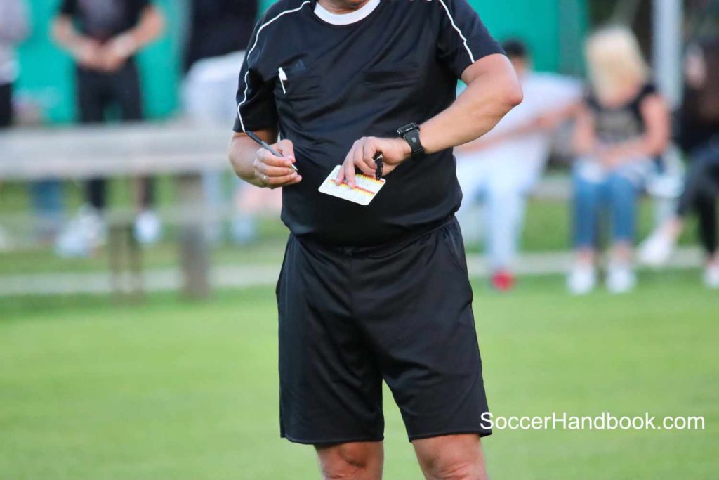 Soccer referee looking entering a player into his book after issuing a yellow card