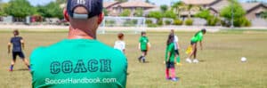 The Soccer Handbook - Coach looking on as youth players practice