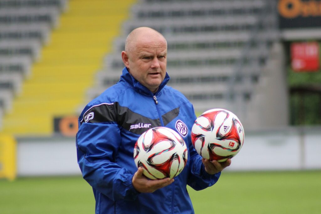 Assistant soccer coach holding two match balls.